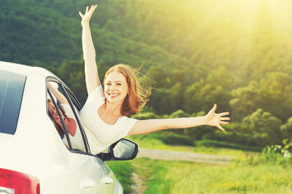 girl-leaning-out-of-car-window-on-raod-with-sunshine-and-fields